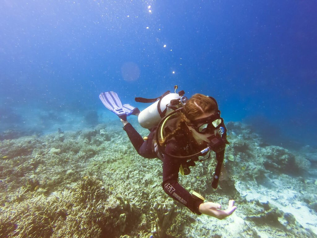 female woman scuba diver checking dive computer over coral reef