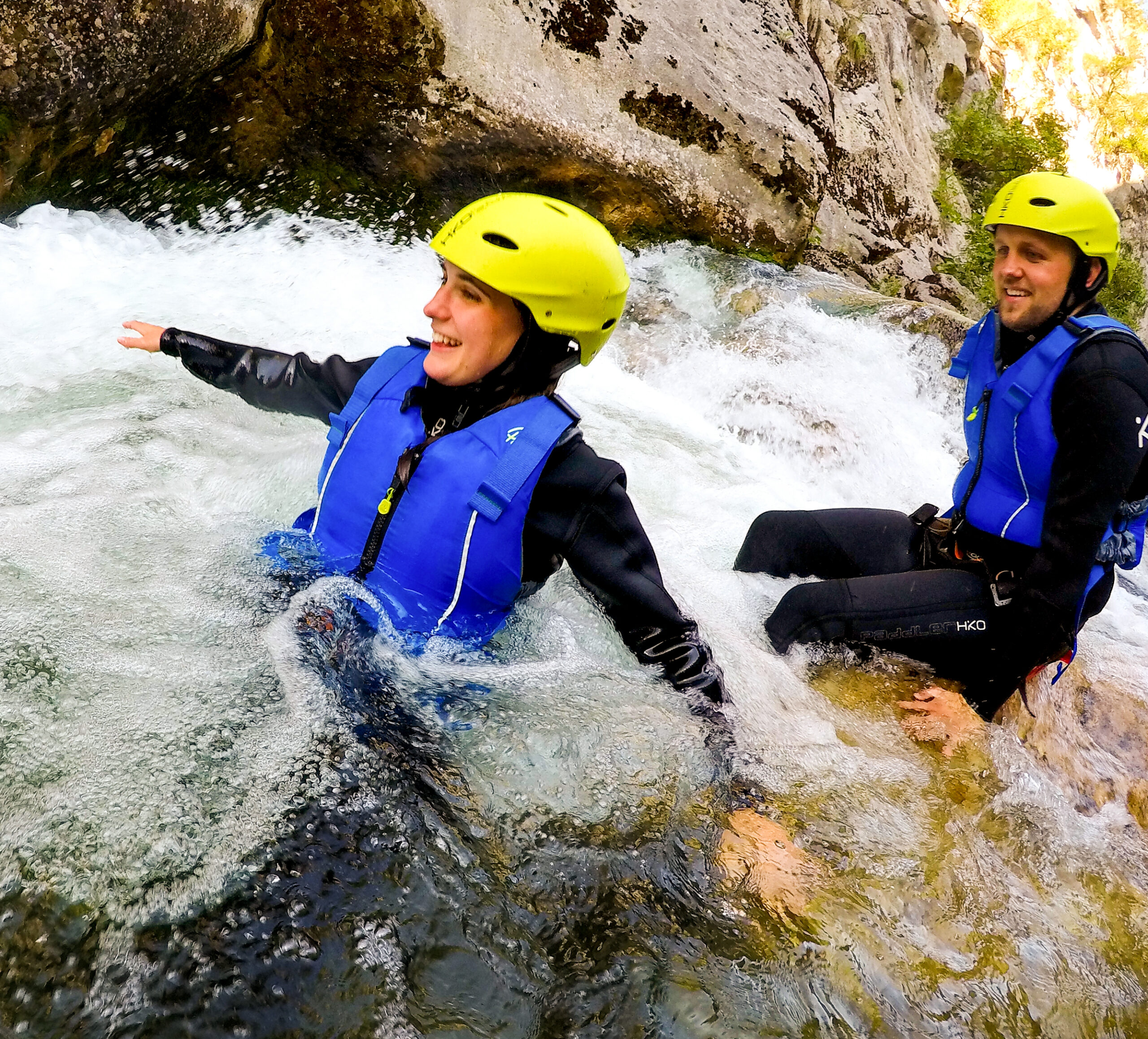 woman canyoning in a river with a yellow helmet and blue life vest