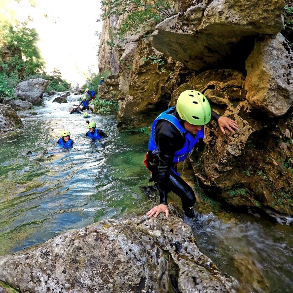 man climbing over rock in river canyoning in blue life vests and yellow helmets