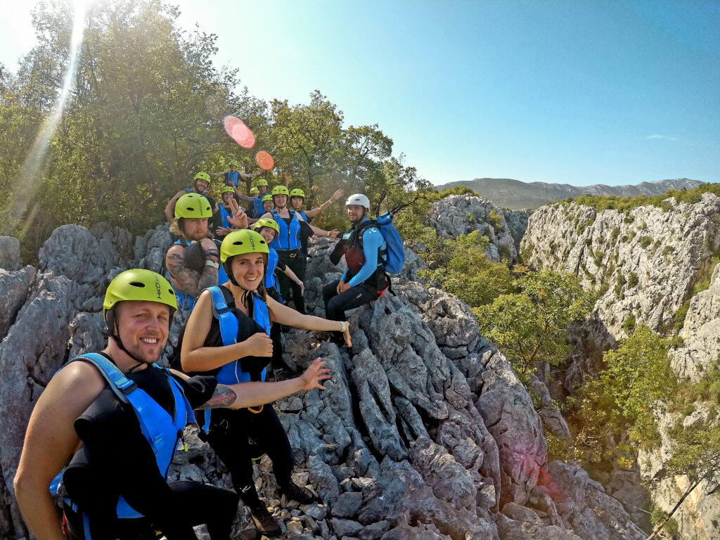 hikers smiling in canyoning gear while hiking along rock in blue life vests and yellow helmets
