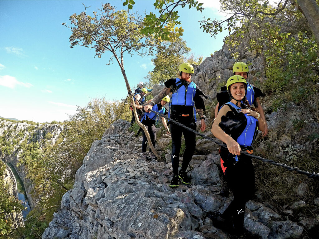 woman walking on a hiking path on a rock edge in a life vest and helmet