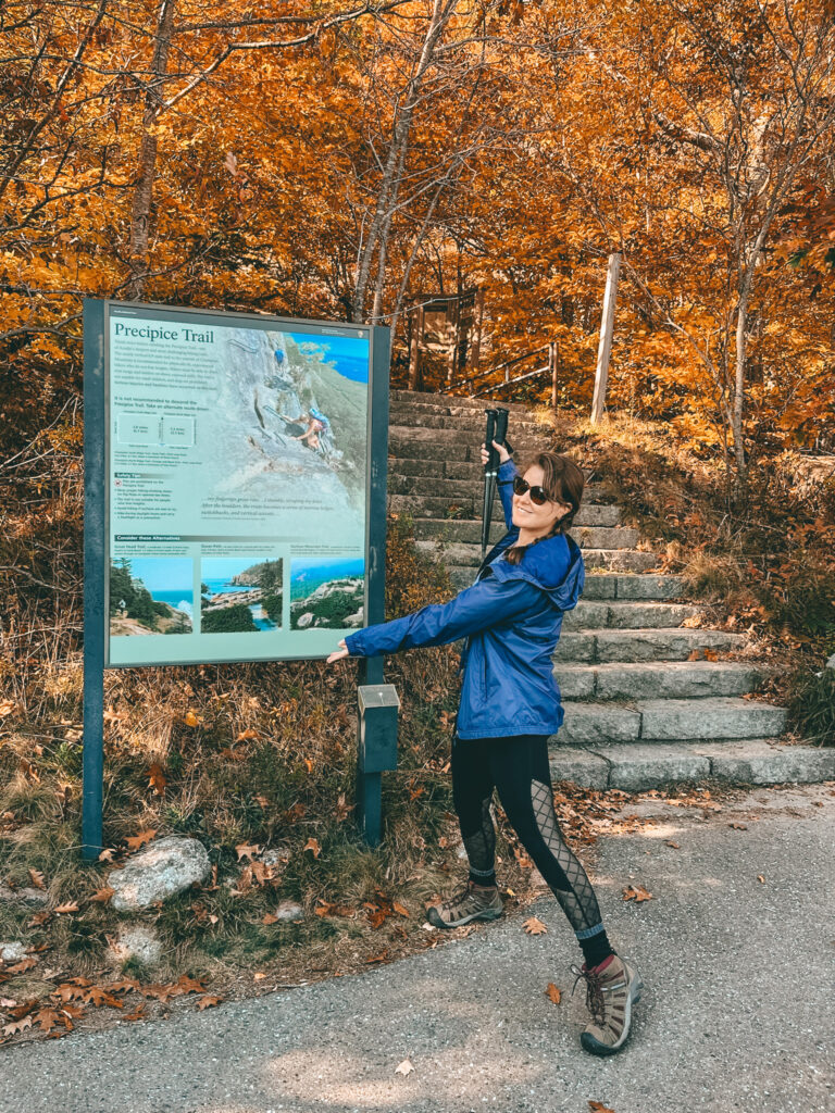precipice trailhead sign with female hiker in blue jacket